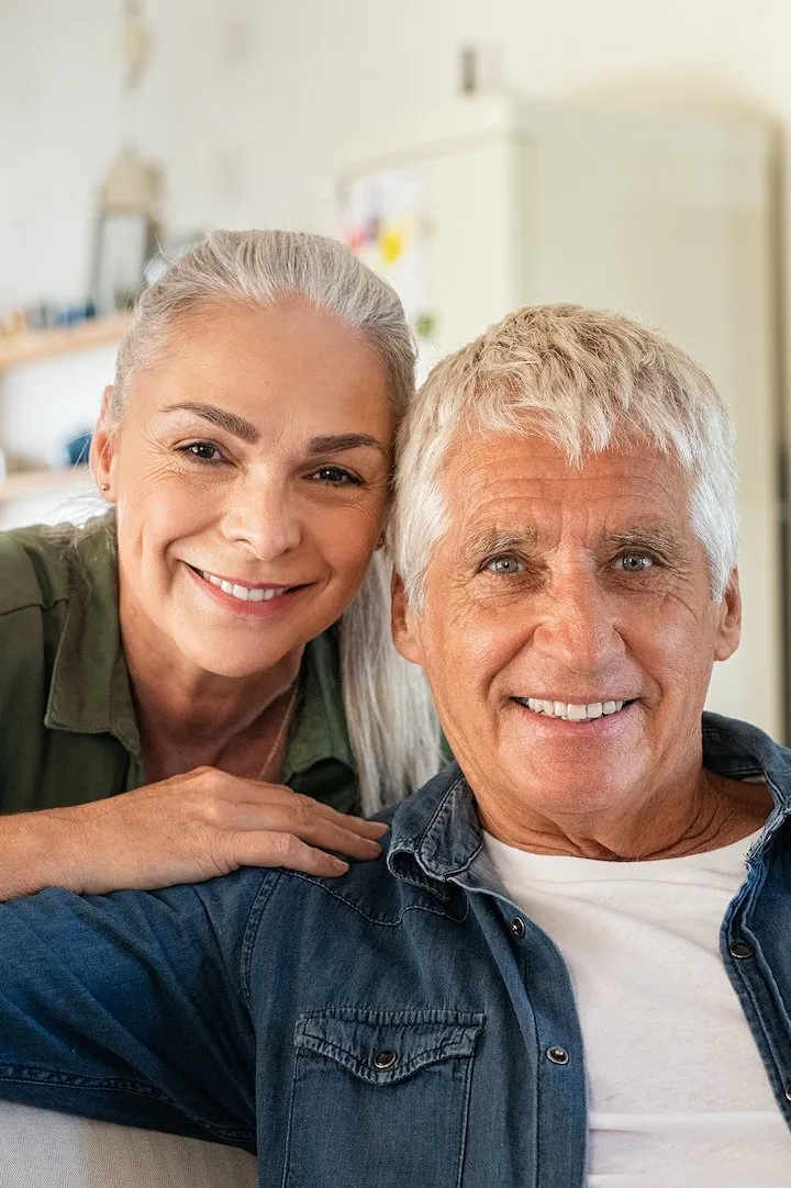 Portrait of happy senior couple relaxing at home and looking at camera. Romantic mature woman embrac